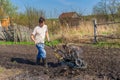 Man in wellingtons with cultivator ploughing ground in sunny day. Farmer plowing kitchen-garden in suburb. Land cultivation, soil
