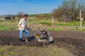 Man in wellingtons with cultivator ploughing ground in sunny day. Farmer plowing kitchen-garden in suburb. Land