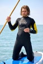 Man in wetsuit standing on paddle board at sea on blue water. Young male model Royalty Free Stock Photo