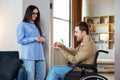 Man in wheelchair extend her hand palm up to side. Woman giving key with keychain from new house for handicapped Royalty Free Stock Photo