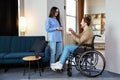 Man in wheelchair extend her hand palm up to side. Woman giving key with keychain from new house for handicapped Royalty Free Stock Photo