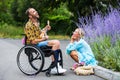 Man in wheelchair outdoors playing the guitar for blond woman sitting at curb Royalty Free Stock Photo