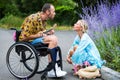 Man in wheelchair outdoors playing the guitar for blond woman sitting at a curbman in wheelchair outdoors playing the guitar for Royalty Free Stock Photo