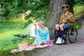 Man in wheelchair playing guitar for blond woman outdoor by a river Royalty Free Stock Photo