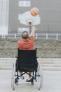 man in a wheelchair plays basketball alone in a city park
