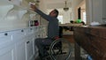 Man in wheelchair reaching out to pack plate ion a shelf in white modern kitchen