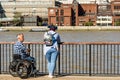 Man in a Wheelchair and A Woman Leaning on a Fence In Conversation Overlooking the River Thames at Bankside London