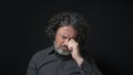 Man with white beard and black curly hair with sad expression, eyes closed and head down, wearing black shirt against black Royalty Free Stock Photo