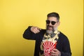 Man with white beard and sunglasses on isolated yellow background holding a large bucket of popcorn while pointing forward Royalty Free Stock Photo