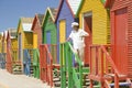 Man with white hat standing in front of bright Crayon-Colored Beach Huts at St James, False Bay on Indian Ocean, outside of Cape