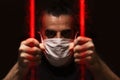 Man with white medical mask standing in the dark, holding red bars made of viruses with his bare hands, locked away in dark