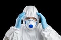 Man in white protective suit holds his head. Man in facepiece respirator and glasses, hands in disposable blue glove