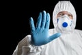 Man in white protective suit showing stop gesture on black background. Hand ind blue glove, palm stop sign Royalty Free Stock Photo