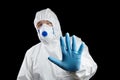 Man in white protective suit showing stop gesture on black background. Hand ind blue glove, palm stop sign Royalty Free Stock Photo