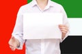 Man with a white sheet of paper in his hands, for your text, mockup. Against the background of the flag of the UAE. Unknown person Royalty Free Stock Photo