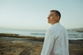 A man in a white shirt against the background of the sea and sunset. A guy is walking on the beach and enjoying the views, Royalty Free Stock Photo