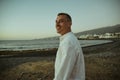 A man in a white shirt against the background of the sea and sunset. A guy is walking on the beach and enjoying the views, Royalty Free Stock Photo