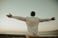 A man in a white shirt against the background of the sea and sunset. A guy is walking on the beach and enjoying the views, Royalty Free Stock Photo