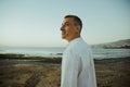 A man in a white shirt against the background of the sea and sunset. A guy is walking on the beach and enjoying the views, Royalty Free Stock Photo