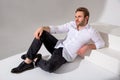 A man in a white shirt, dark jeans and black boots sits against a plain background and looks forward. Casual wear. Confident look Royalty Free Stock Photo