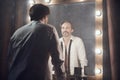 Man in white unbuttoned shirt with balck tie in front of mirrow with lights looking at own reflection Royalty Free Stock Photo