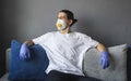 Man in white shirt, medical mask and rubber gloves is sitting on a sofa and feeling great staying home while pandemic Royalty Free Stock Photo