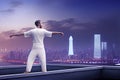 Man in white shirt practicing qigong outdoors, twilight city scape background