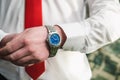 A man in a white shirt and red tie puts a wristwatch on his arm