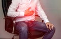 A man in a white shirt is sitting on a chair and holding on to the stomach, abdominal pain, heartburn