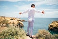 Man in white shirt stands on the edge of the abyss and enjoy the ocean with raised hands . Royalty Free Stock Photo