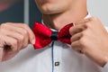 A man in a white shirt ties a red bow tie while preparing for a wedding ceremony Royalty Free Stock Photo