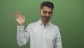 Man in white shirt waves bare hand and smiles in bright green studio; friendly welcome open communication Royalty Free Stock Photo