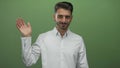 Man in white shirt waves bare hand and smiles in bright green studio; friendly welcome open communication Royalty Free Stock Photo