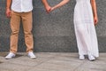 Man in white shirt and woman in white dress holding hands of each other while standing near the grey wall. Royalty Free Stock Photo