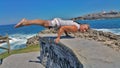 man in white shorts and white t-shirt does gymnastic exercise on a stone wall against a blue sea