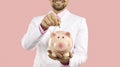 Happy young businessman who's investing or saving money puts coin in his piggy bank Royalty Free Stock Photo