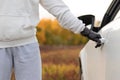 A man in a white sweater and black gloves opens the car door to steal him on a warm autumn day