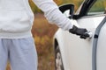 A man in a white sweater and black gloves opens the car door to steal him on a warm autumn day. Selective focus