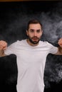 Man in white t-shirt on black background releasing a cloud of smoke