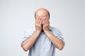 Man in white t-shirt covering his face with hands over white background.