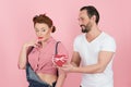 Man in white t-shirt gives beautiful brunette pin-up girl in denim a gift box with ribbon in the form of red heart. Royalty Free Stock Photo