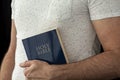 A man in a white T-shirt holds a bible in his hand.