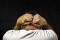 A man in a white T-shirt holds his hands behind his head. Closeup on black background. Royalty Free Stock Photo