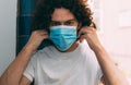 A man in a white T-shirt removes a medical mask from his face, holds her hands by the straps.