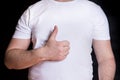 Man in a white t-shirt shows a sign okay with a hand gesture, thumbs up. Man on a black background. Royalty Free Stock Photo