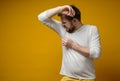 Man in a white t-shirt sniffs his armpits, annoyed by the problem of foul perspiration and body stench. Copy space.