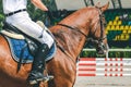 Man in white uniform and sorrel horse at show jumping competition.