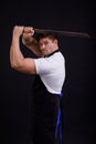 A man holds a machete over his head on a black background