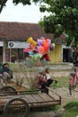 A man who is selling hot air balloons for sale to children who are playing in the city park