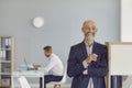 Positive elderly chief company executive standing in office looking at camera and smiling